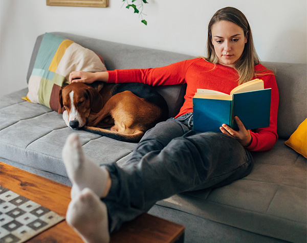 Woman reading a book, with dog lying next to her on sofa in living room