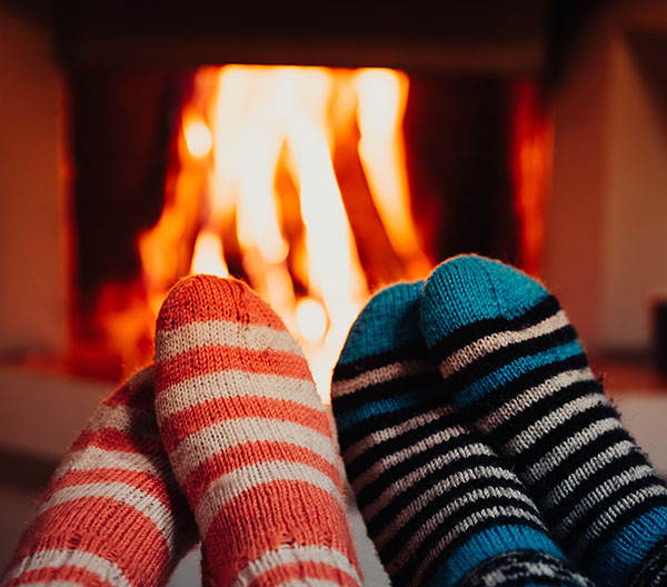 Two pairs of feet in striped socks warming in front of a fireplace